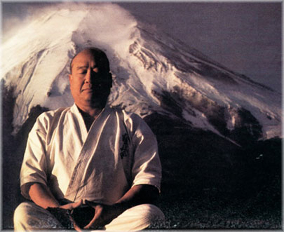Mas Oyama sitting in front of a snowy mountain
